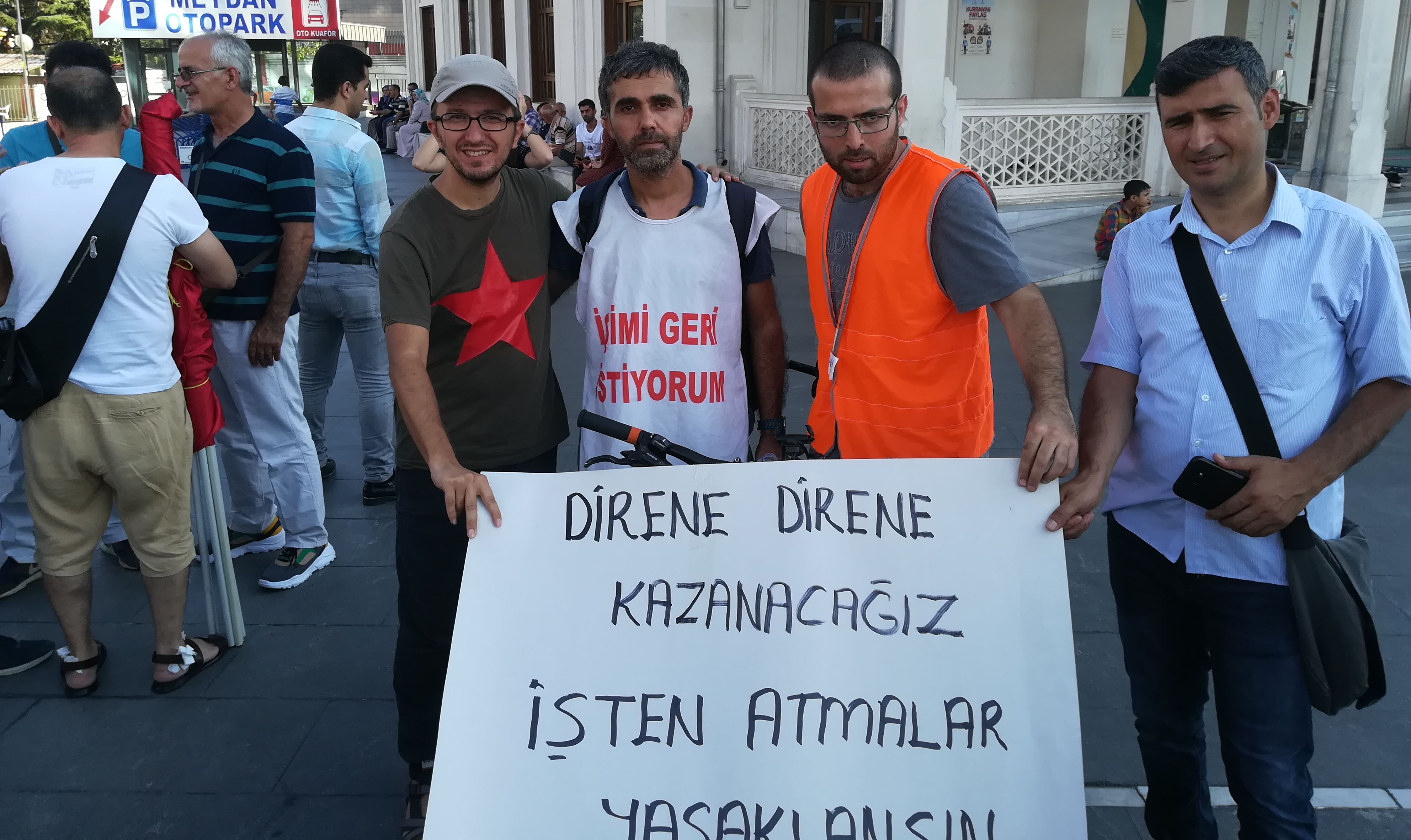 Orhan Esen, Çağrı Gökçek ve KHK ile ihraç edilen Zeytinburnu Belediyesi işçisi Kenan Güngördü ile birlikte "Direne Direne Kazanacağız. İşten Atmalar Yasaklansın" pankartı önünde fotoğraf çektirirlerken.